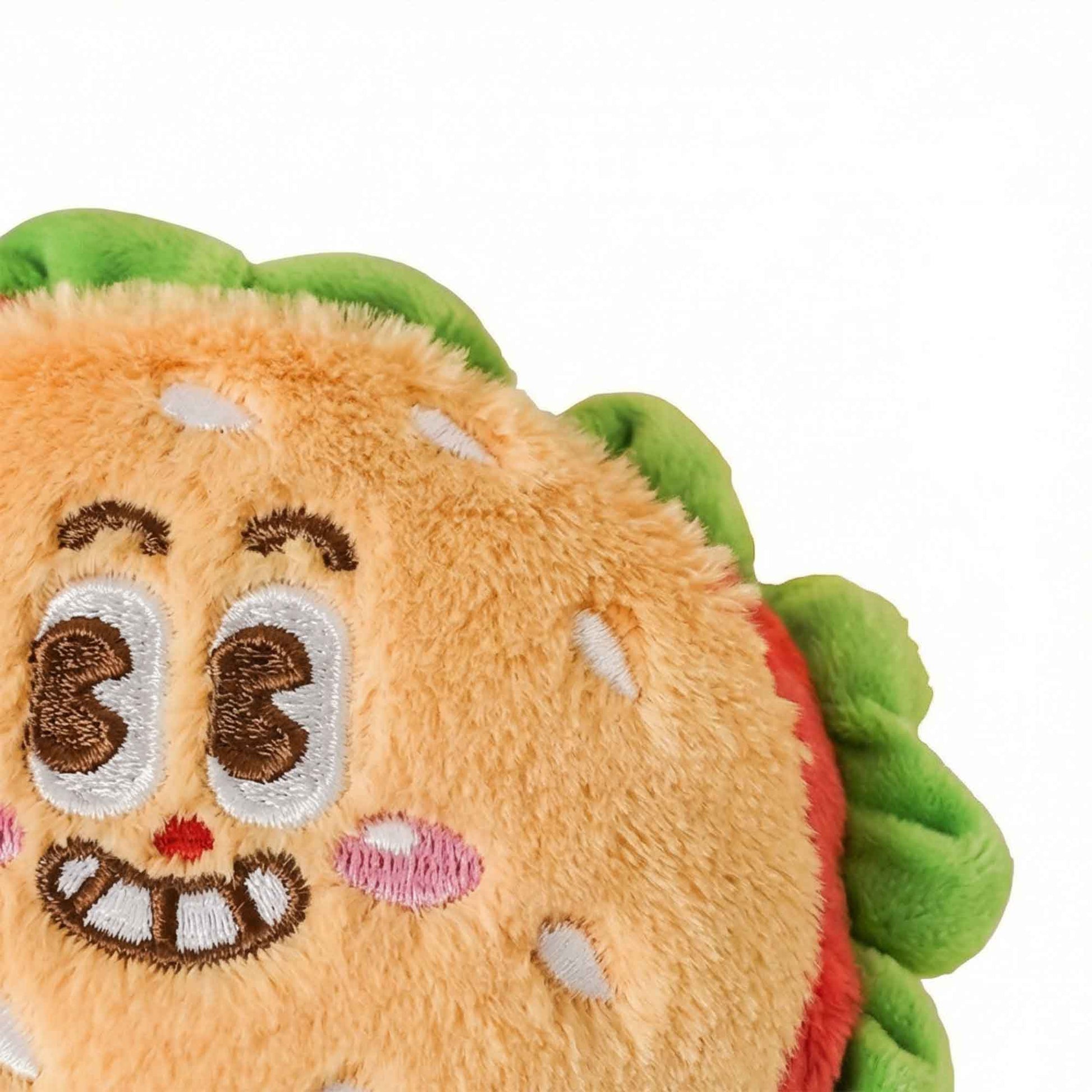 Close-up of cute burger plush dog toy embroidered face – happy goofy expression with sesame bun detail and green lettuce edge on ultra-soft squeaky plush by PetsFave