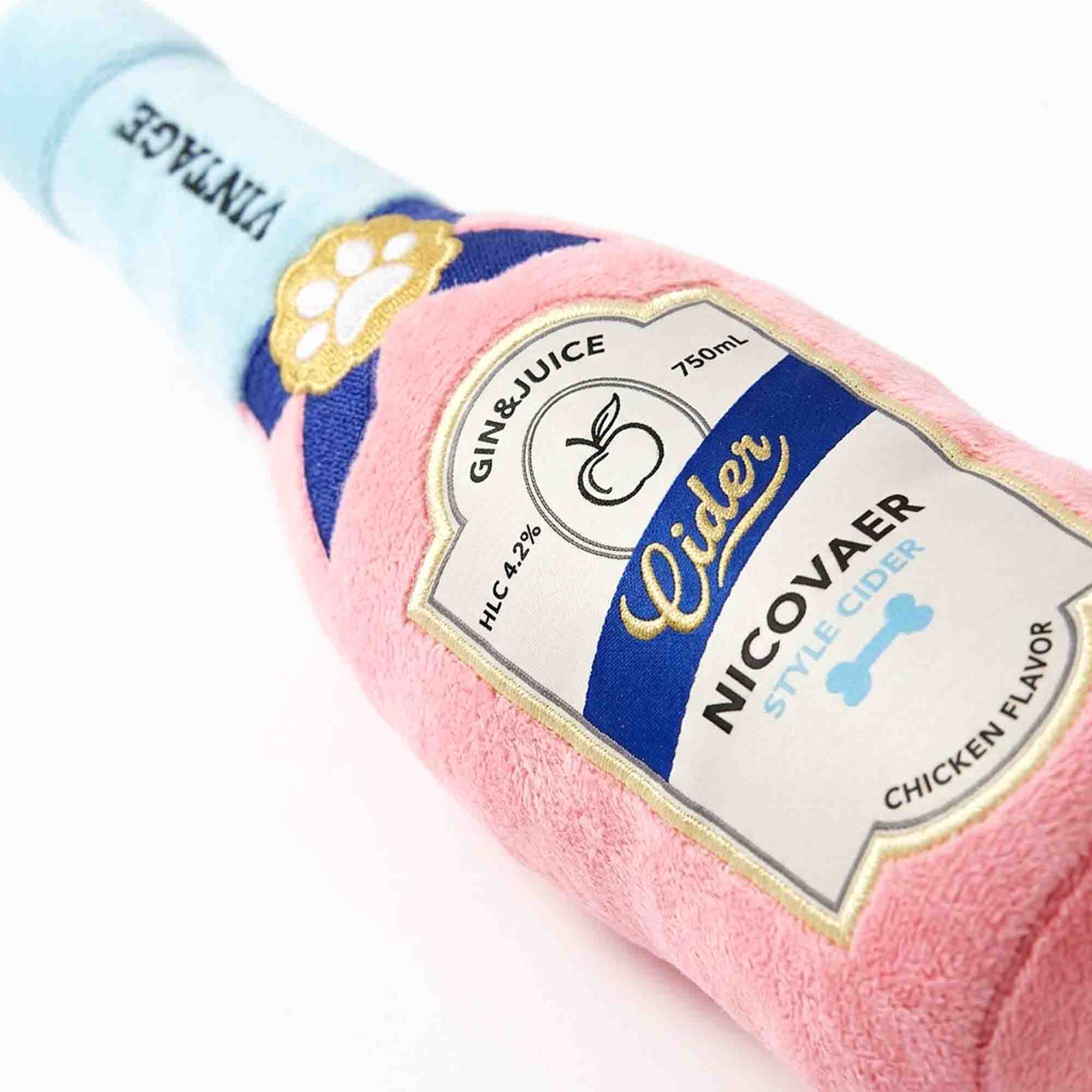 Close-up of pink cider bottle plush dog toy label – detailed embroidered with paw print and chicken flavor parody on soft squeaky plush by PetsFave